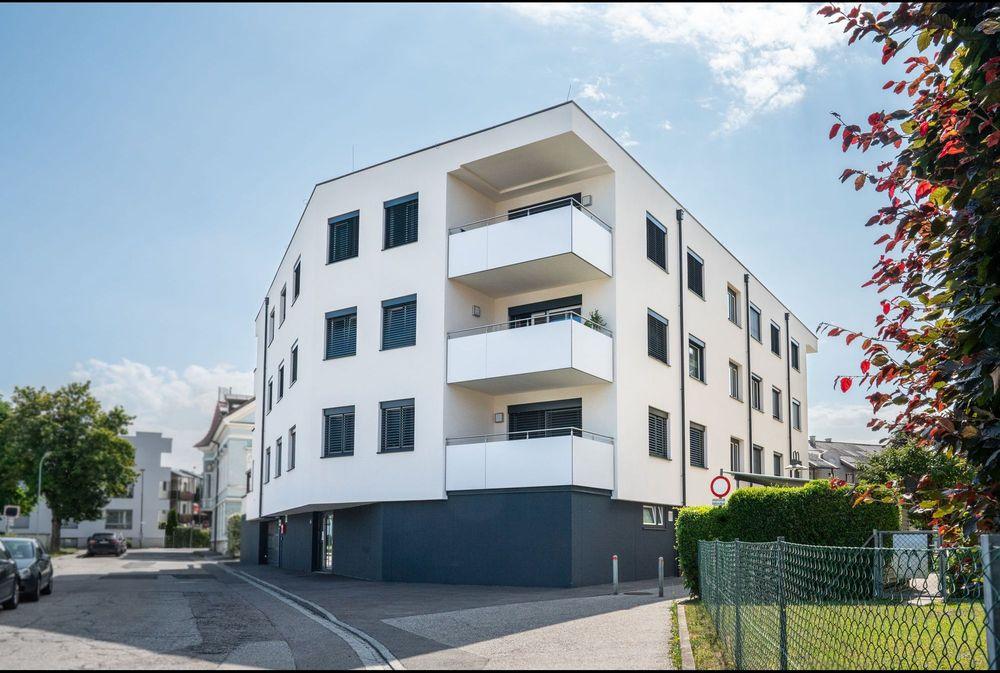 Fabrikssteig 15 - Willkommen in unserem modern und elegant gestalteten Wohnanlage, die von uns als Bauträger errichtet und verkauft wurden. Dieses Bild zeigt das schöne Äußere der modernen Gebäude, umgeben von Grün und Bäumen. Im Hintergrund können wir den klaren blauen Himmel und eine ferne Stadtlandschaft sehen. Diese Wohnanlage bietet luxuriöse Wohnräume, hochmoderne Annehmlichkeiten und eine friedliche Umgebung, die die Bewohner ihr Zuhause nennen können.